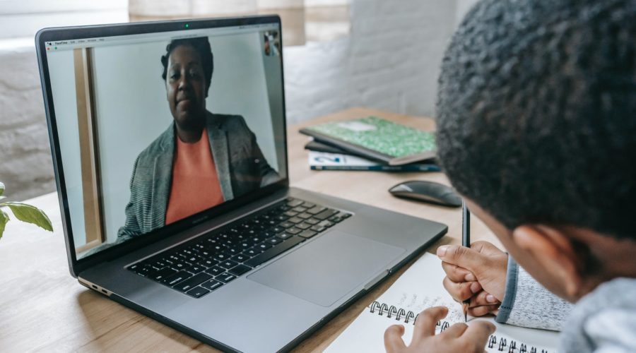 diligent black boy writing exam while teacher dictating online